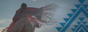 Adult Native American wearing full traditional dress performing a ceremonial dance.