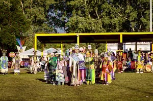 A line of Native American women wearing traditional dress at a Pow Wow.